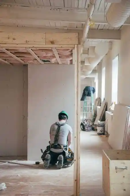 Worker installing drywall and interior framing in a commercial office renovation project.