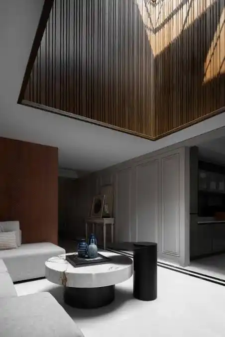 Modern interior design featuring a luxurious double-height living room with wooden ceiling panels, minimalist furniture, marble coffee table, and natural lighting.